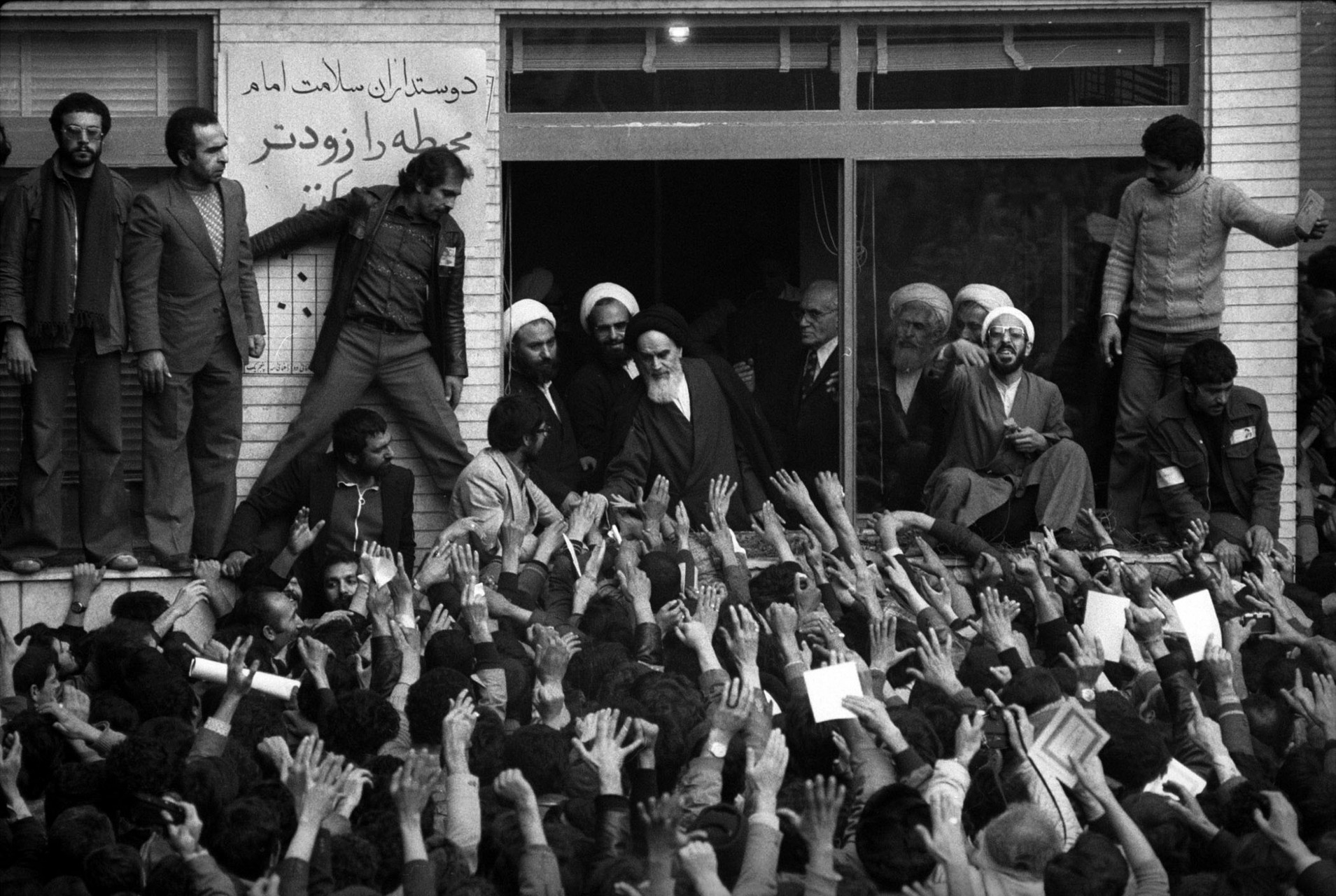 Ayatollah Khomeini salutes the crowds from his small school room office.