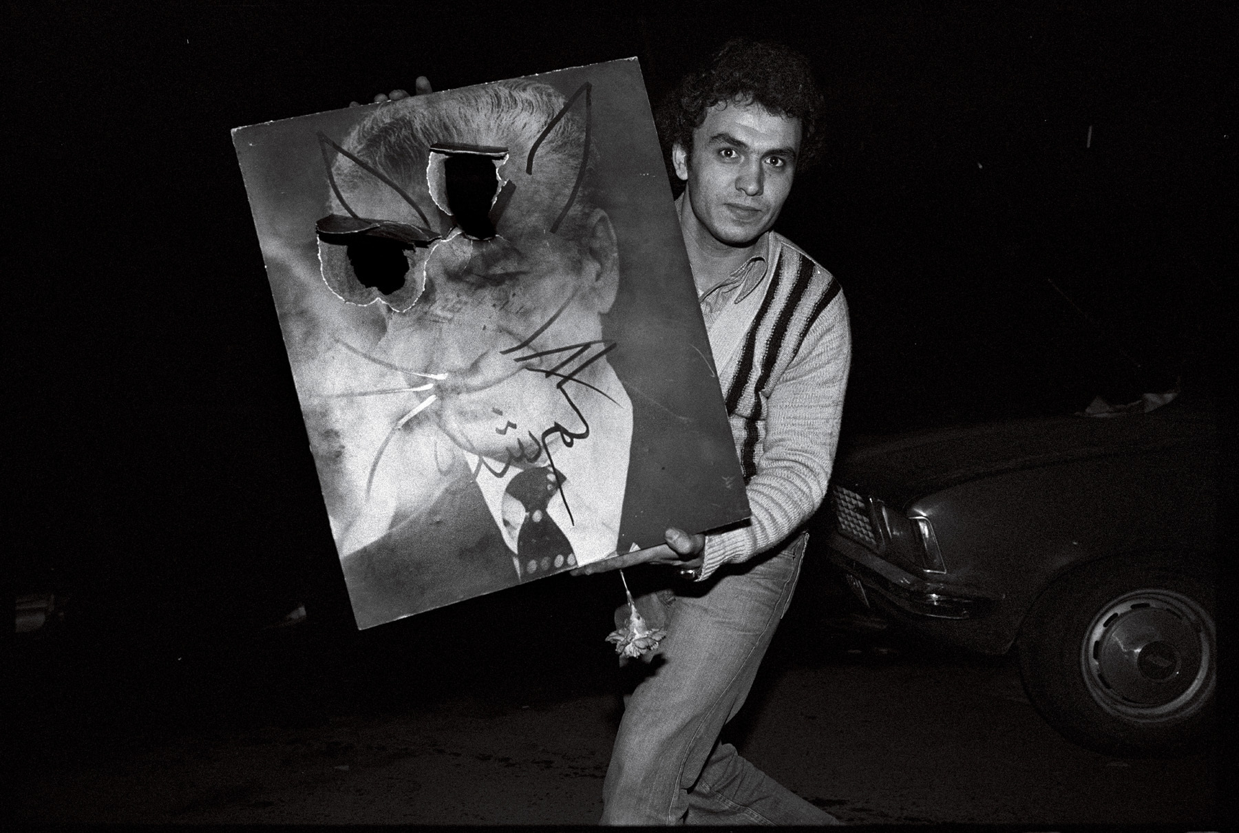 A young man displays a defaced portrait of the Shah.