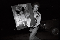 A young man displays a defaced portrait of the Shah.