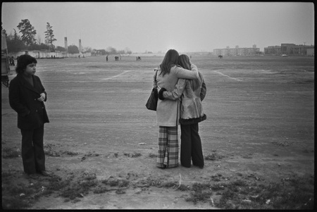 Outside the stadium, two young women comfort each other as they fail to get information about loved ones, as prisoners at the stadium.